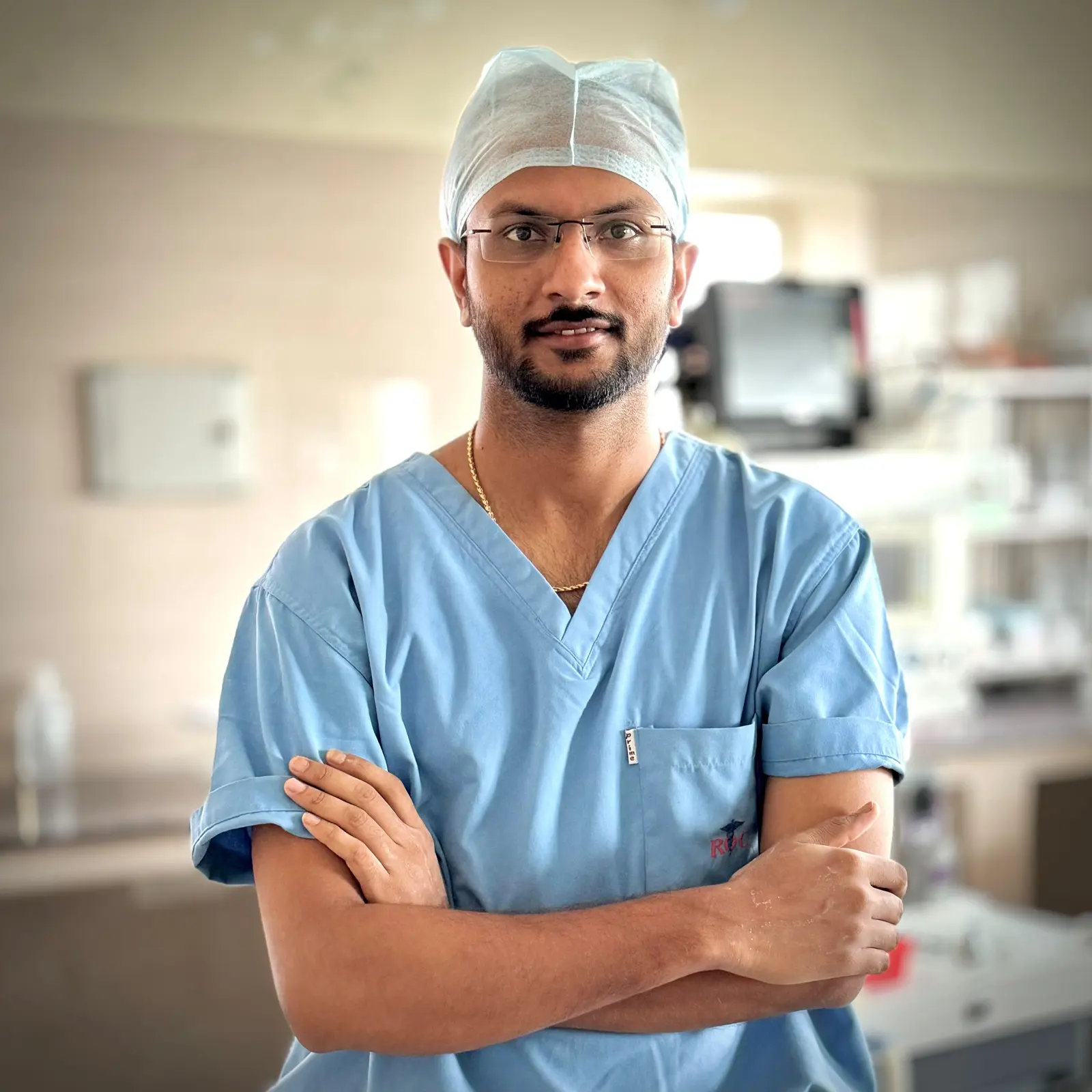 Dr. Balagangadhara Choudhary V in surgical scrubs, arms crossed, facing the camera