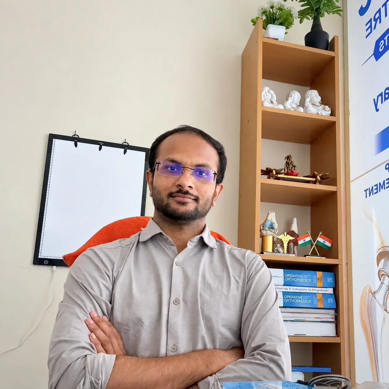 Dr. Balagangadhara seated in the clinic beside orthopaedic textbooks